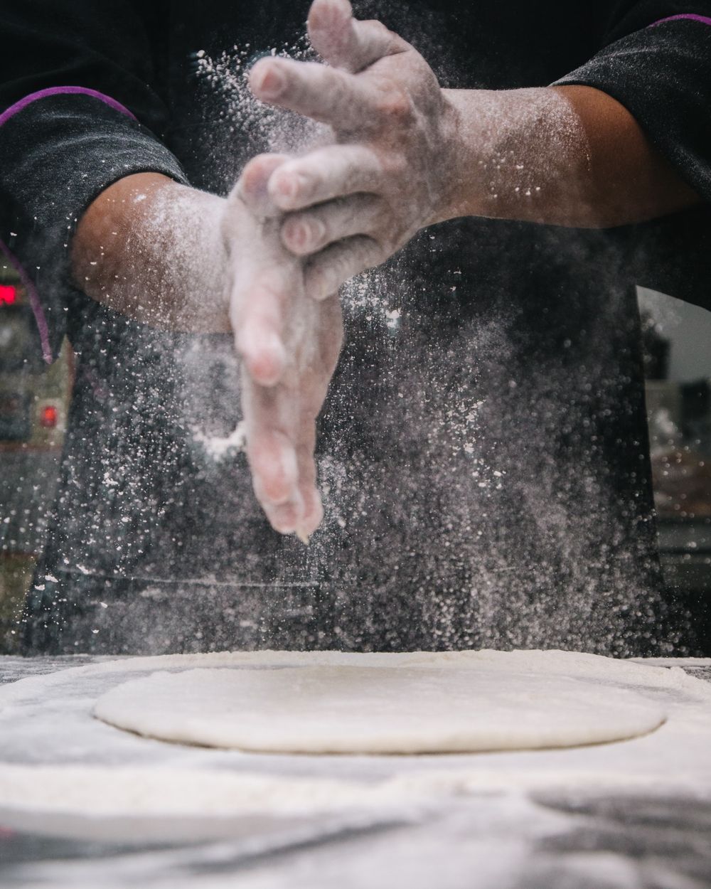 Mãos enfarinhadas abrindo massa sobre a bancada de uma cozinha profissional